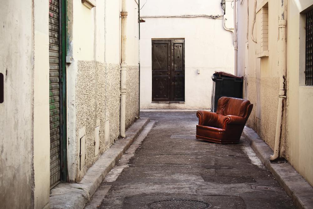 An abandoned armchair in a tight alley photographed in Italy. Symbolic color street photography.