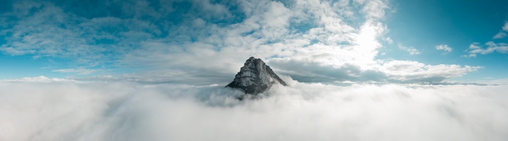 An image of a mountain peak that is just cresting a low lying formation of clouds.