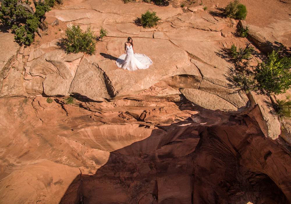 A drone image captures a bride standing on a cliff in a desert. 