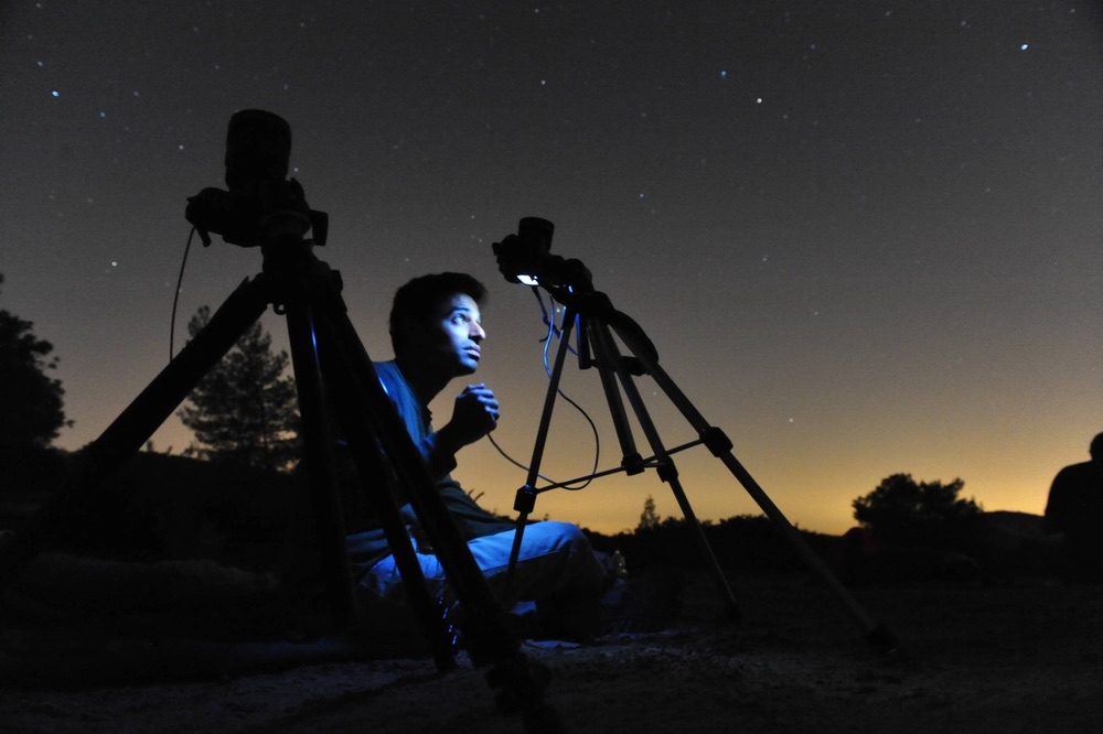A young astrophotographer observing the night sky with the help of a pair of tripods.