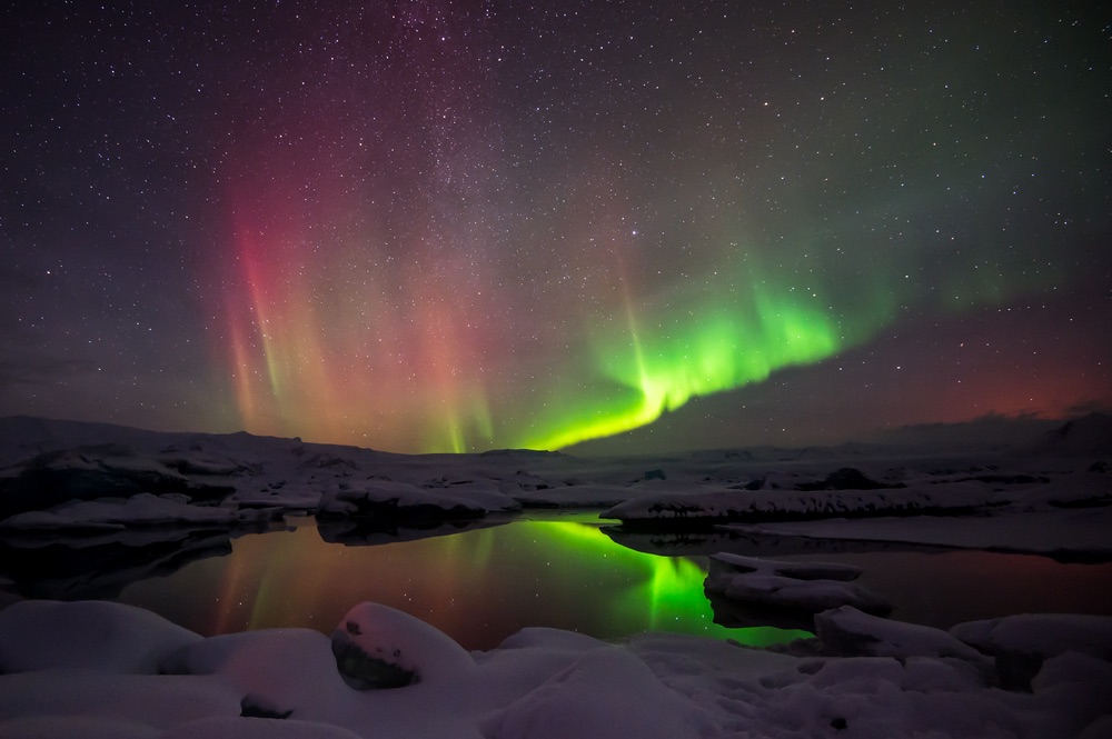 Red-toned northern lights reflected in a still lake — Jokulsarlon Lagoon, Iceland.
