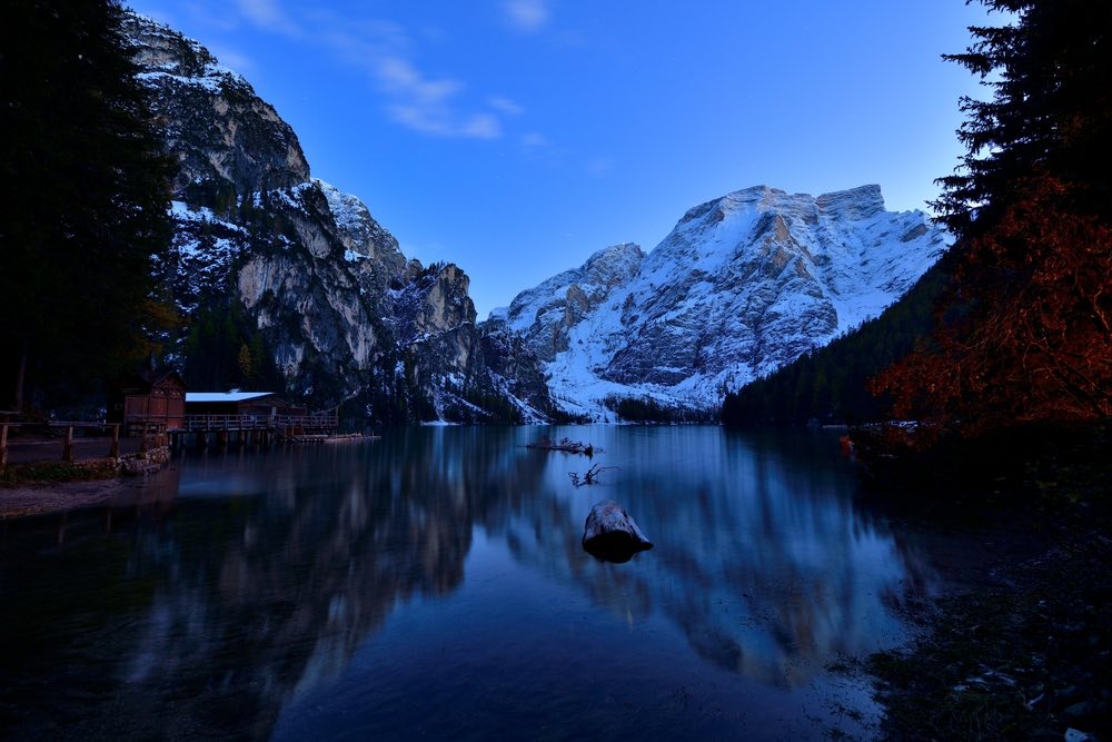 A blue hour landscape shot of a mountains with a river running between them. On the side is a house and a dock.