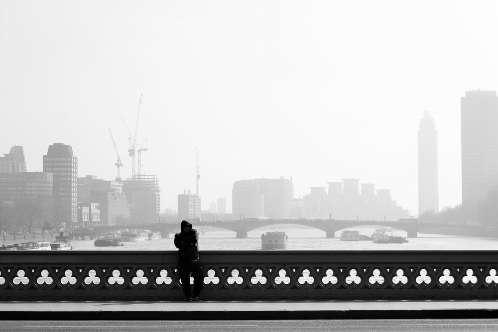 Black-and-white cityscape shot of a lone pedestrian on a bridge. Atmospheric photography showcasing composition and framing.