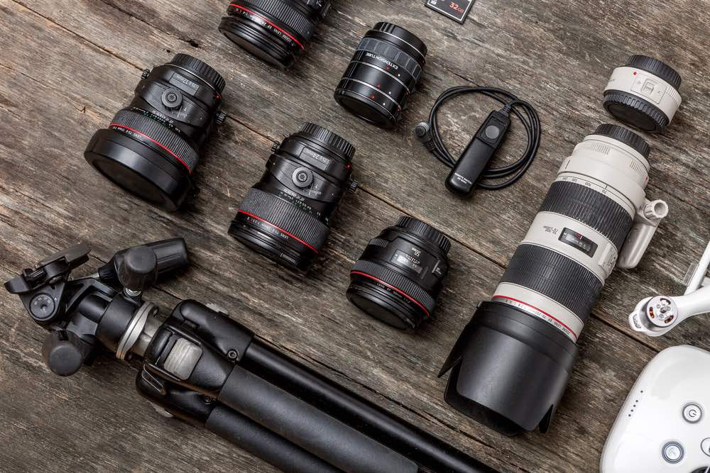 A selection of lenses among other items of photography gear laid out on a wooden surface. Zooms and prime lenses for wedding photography.