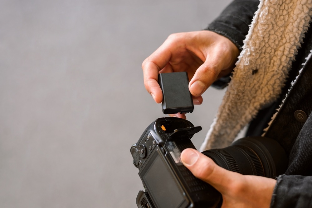 A photographer loading a fresh battery into their mirrorless camera. Close-up view.