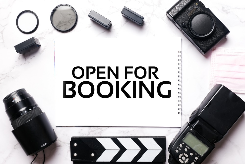 Various pieces of camera equipment surrounding a sign that says "open for booking".