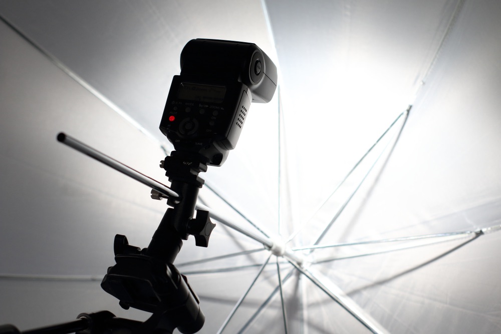 A close-up image of a camera flash shooting into an photography umbrella so the light reflects back softer.