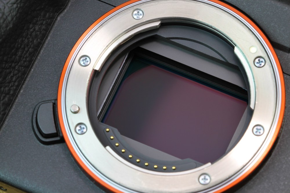 A close-up view of a contemporary digital camera CMOS sensor. Lens mount and electronic contacts visible.