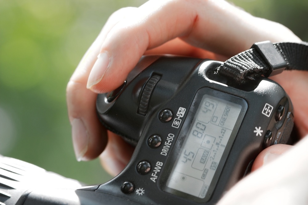 Adjusting camera exposure settings via buttons and dials. Close-up view of top LCD area of a Canon DSLR, showing many essential controls.