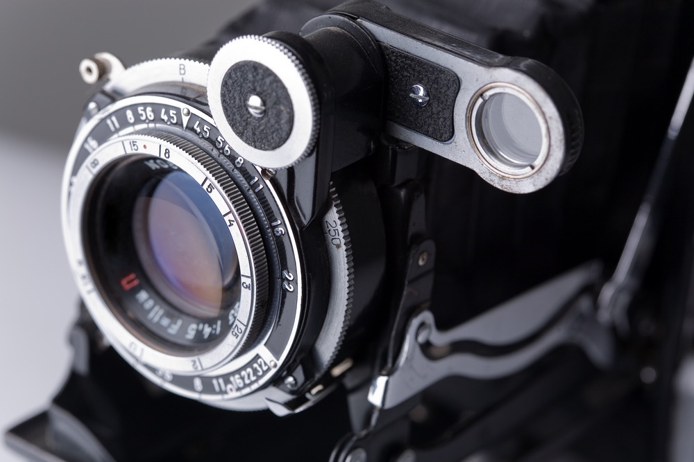 Close-up view of a vintage medium-format camera showing the all-manual exposure controls on the lens barrel. Shutter speed, aperture, focus, and shutter release controls.