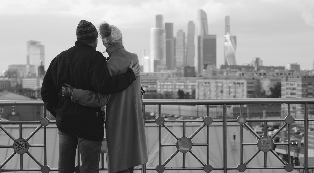 A couple embracing by a cityscape view. Black-and-white street photograph.
