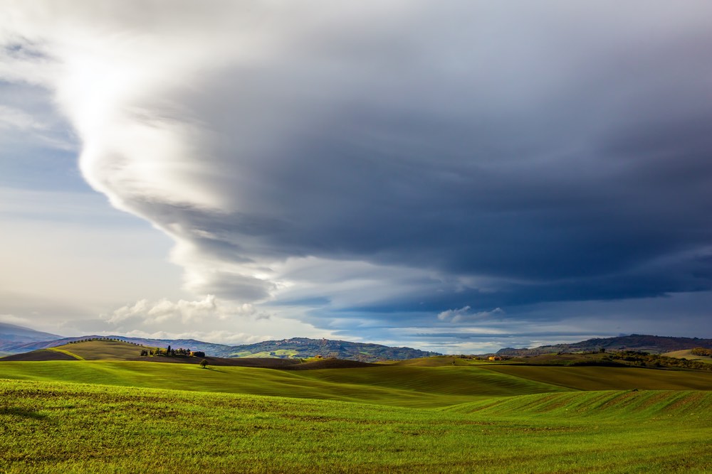 A landscape photo of a field with some dramatic looking clouds above it. 