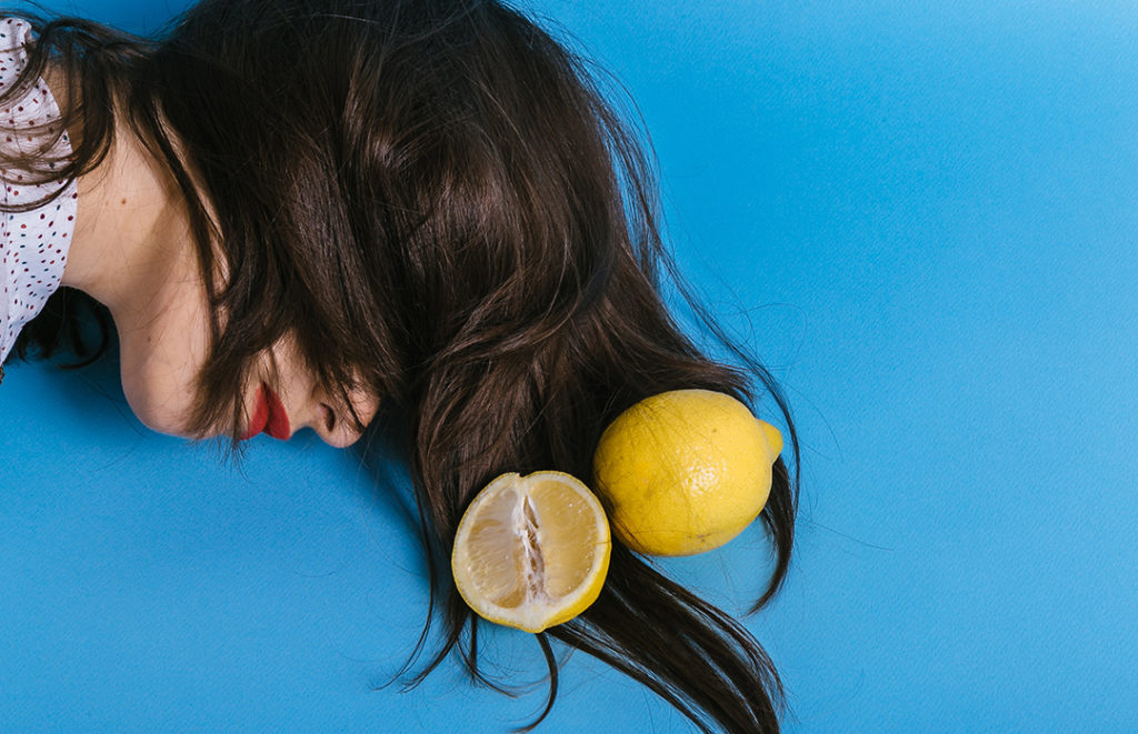 inspiring conceptual shot of woman lying next to two lemons in front of a blue background