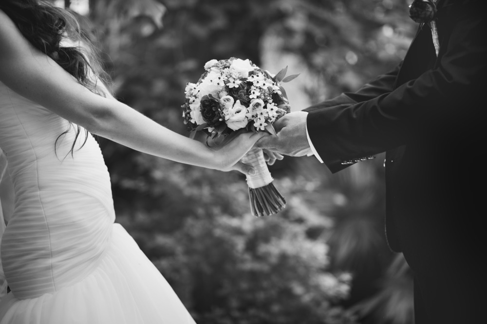 A B&W image of a bride and groom holding the bouquet together.
