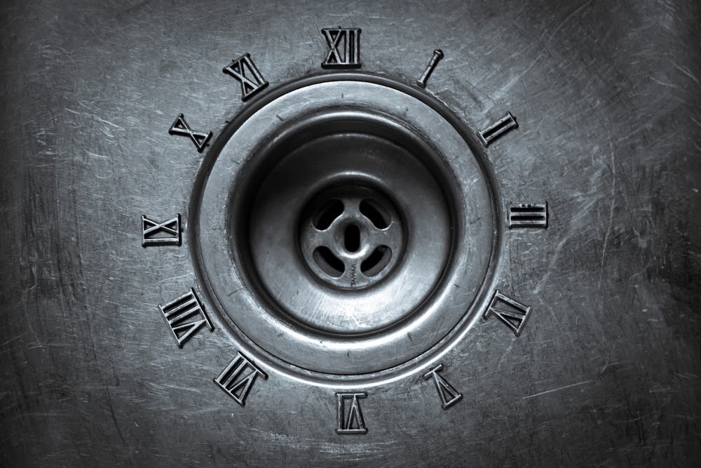 Close-up view of an ordinary kitchen sink drain with a ring of Roman numerals around it. Concept photography discussing motifs of time and passage.