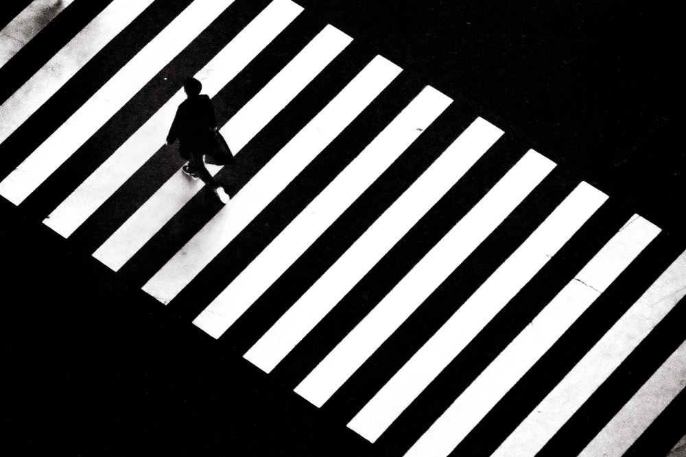 A man crossing a street. Black-and-white street photography composition which may be dubbed a 'decisive moment' capture.