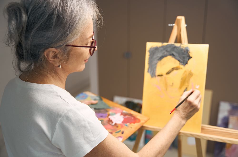 elderly woman painting calmly with a brush indoors.