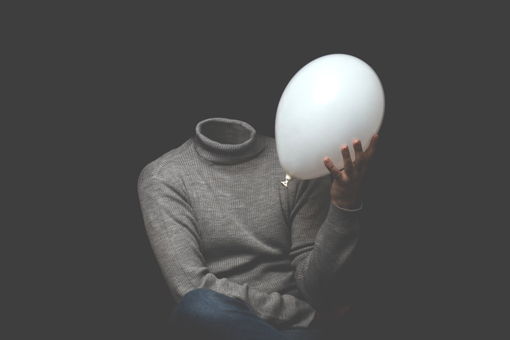 A headless person wearing a turtleneck sits holding a balloon in their hand. 
