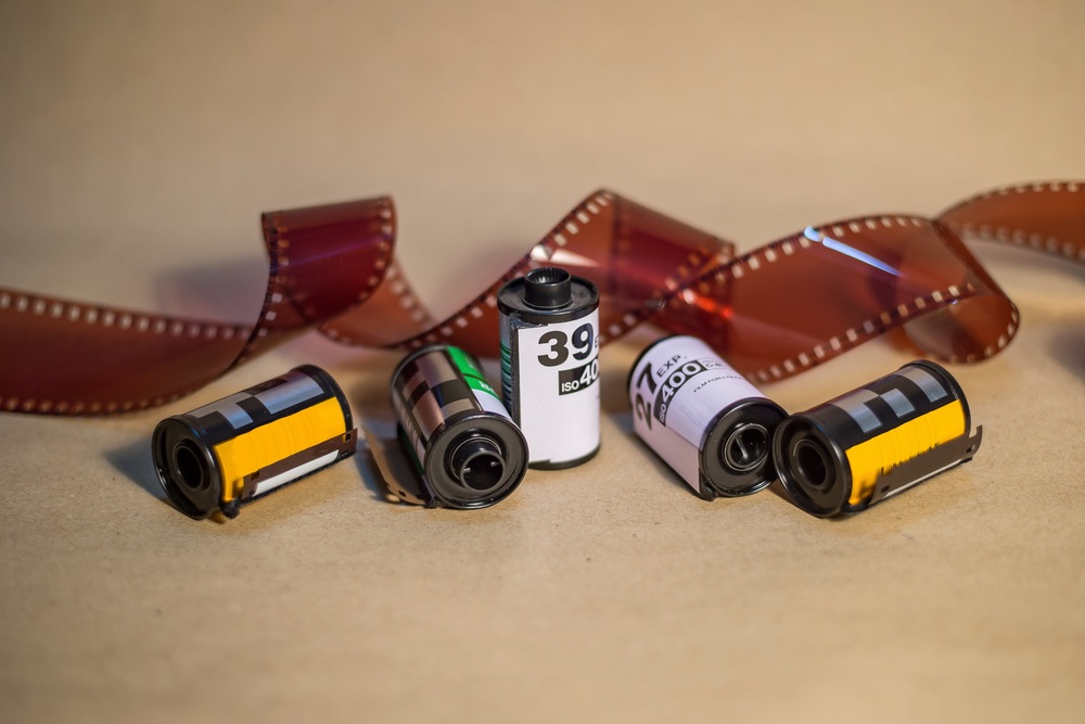 A few rolls of 35mm film in their cartridges, with an unwound strip of film in the background. Analog photography.