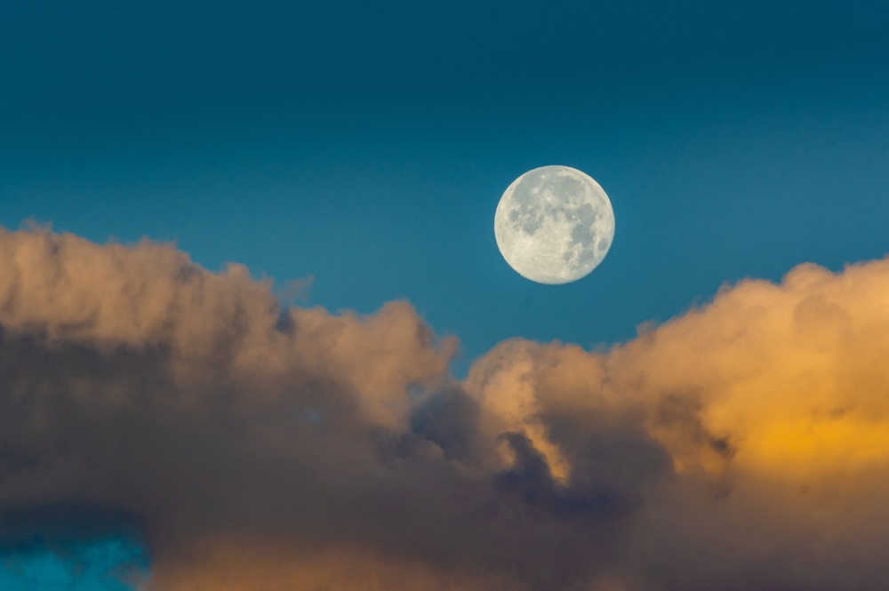 clouds juxtaposed against a daytime sky with a full Moon.