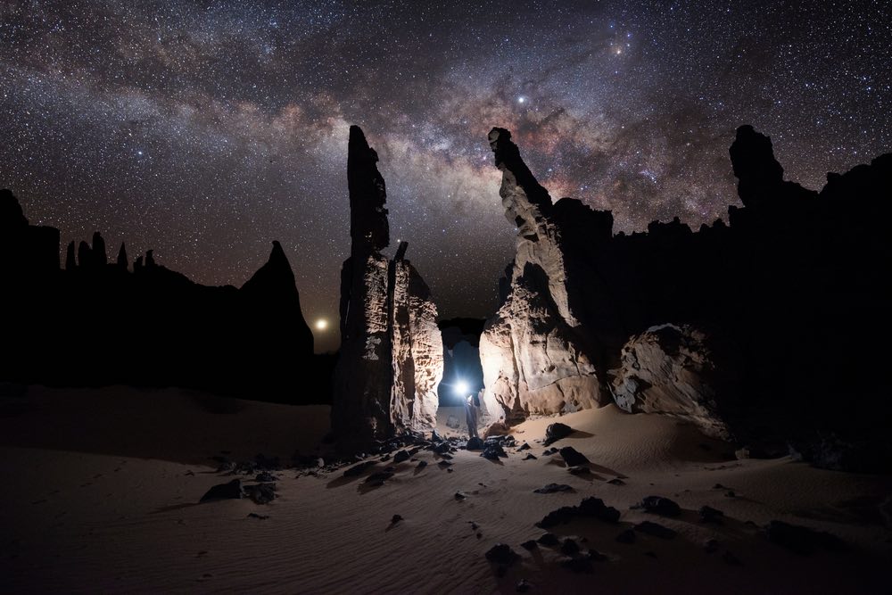 Astrophotography of the Milky Way with rock fomation in front and person holding a torch.