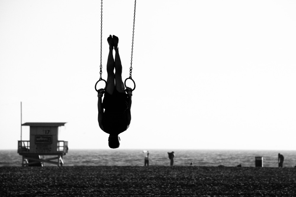 A gymnast practicing on rings at a beach. Black-and-white sports photography.