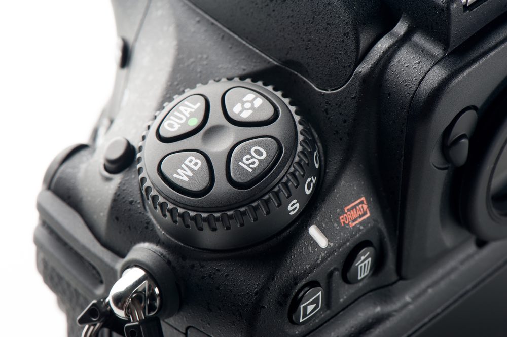 Close-up view of a DSLR camera's ISO dial. Metering mode, white balance, and quality buttons visible.