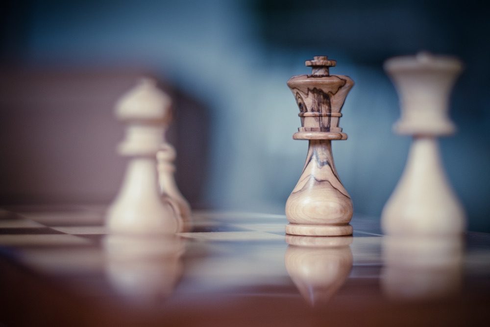 A set of chess pieces in close-up view. Focus set on the white king, with surrounding subjects selectively blurred.