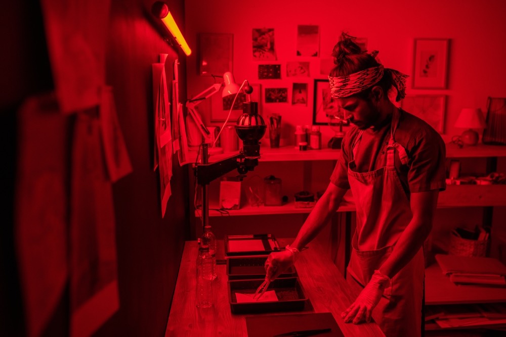 Scene of a young man using tongs in a darkroom. Traditional photographic printing process illustrated in color.