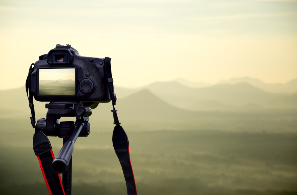 A camera sits on a tripod facing out into a landscape that is foggy and mysterious.