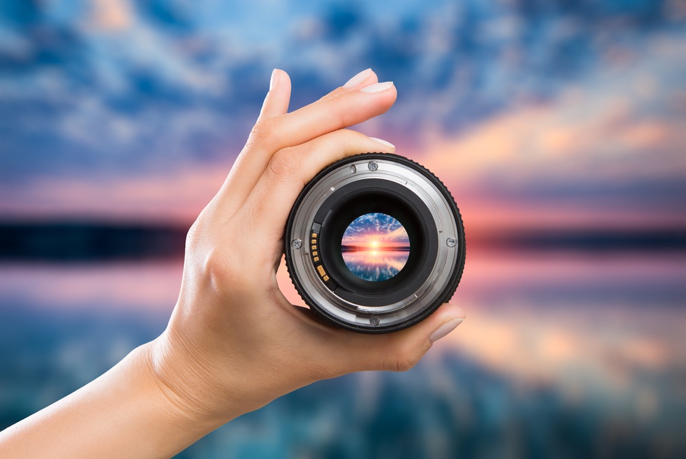 A lens detached from its mount, held in focus over a seaside landscape. A demonstration of focus depth when viewing a scene through a high-power lens.