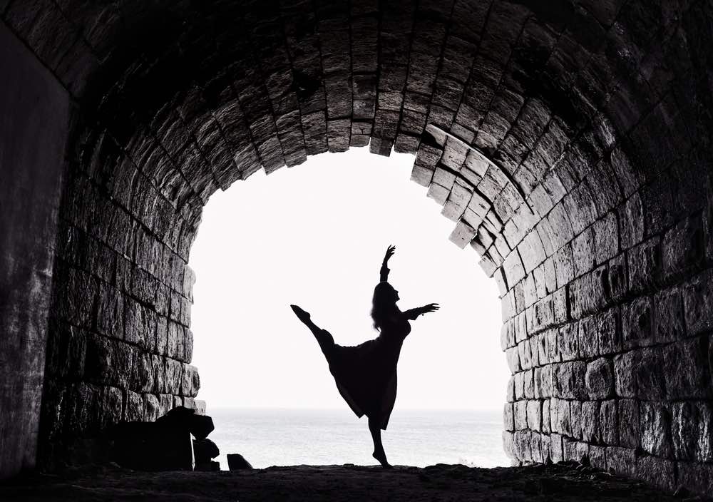 Figure of a dancer against bright white backdrop. Stonewall tunnel as a framing element. Black-and-white photography.