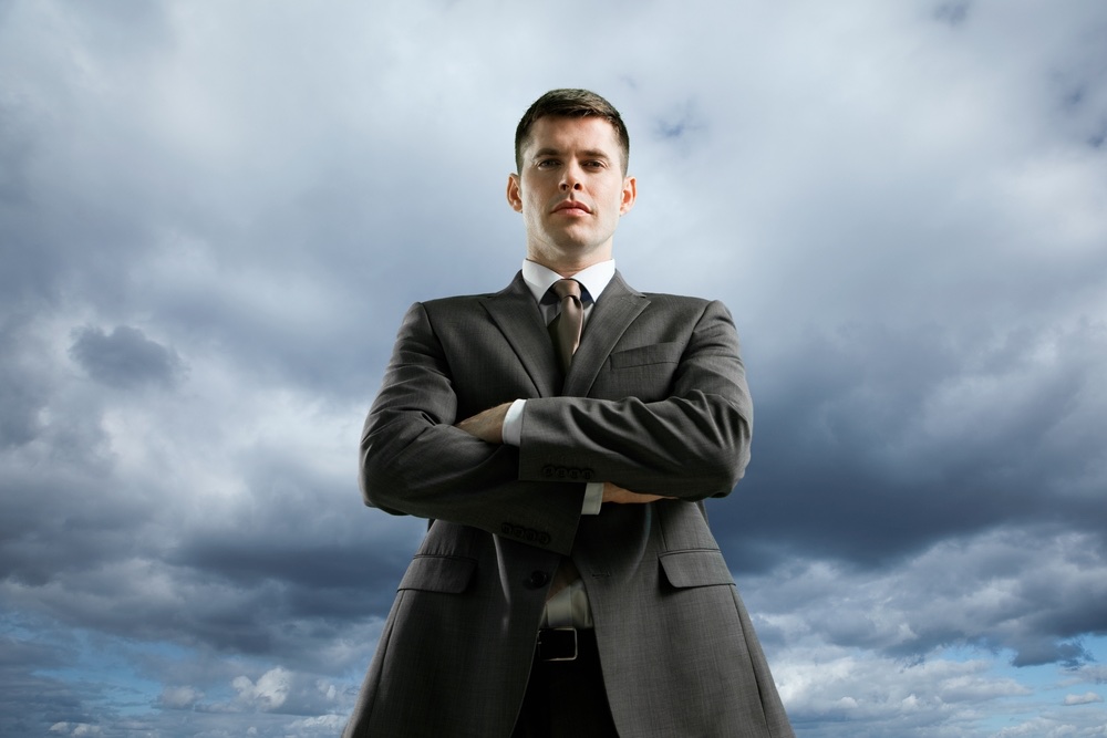 Portrait of a young professional in a dark grey suit. Cloudy sky background. Low-angle portrait photography.