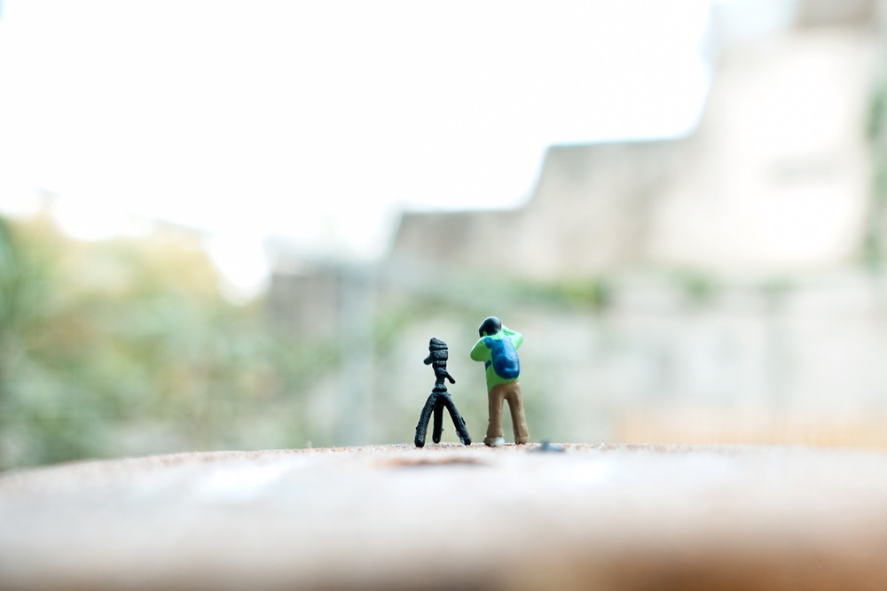 A miniature figurine depicting a photographer lining up a shot using a tripod. Self-referential miniature photography with a dash of humor.