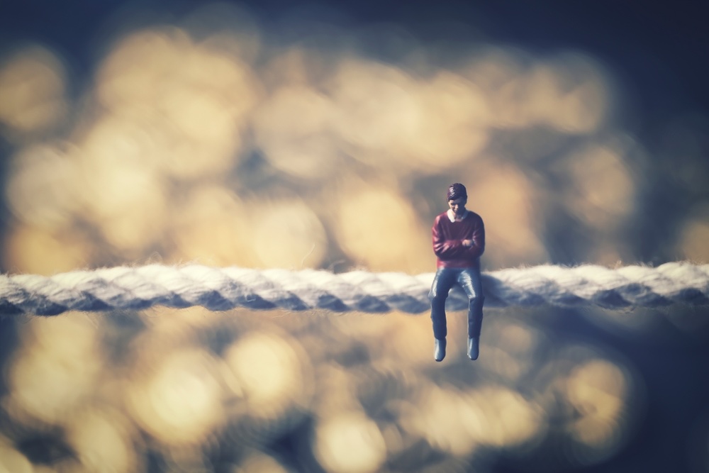 A miniature figure of a man sitting on a rope, contemplating. Strong bokeh achieves background separation and moody atmosphere.