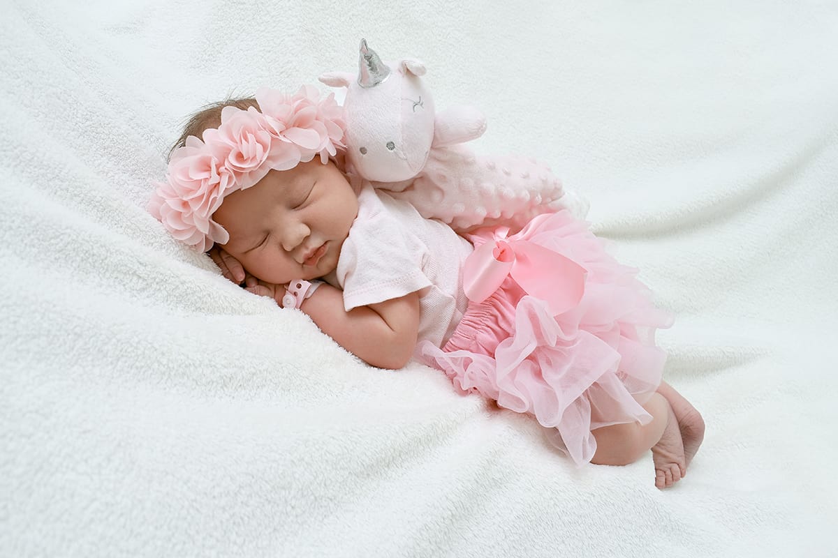 newborn photo ideas baby lying next to unicorn toy.