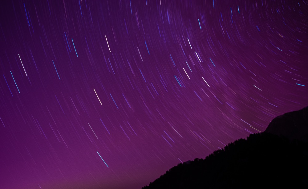A long exposure of the night sky, displaying expressive light trails caused by the movement of the stars.