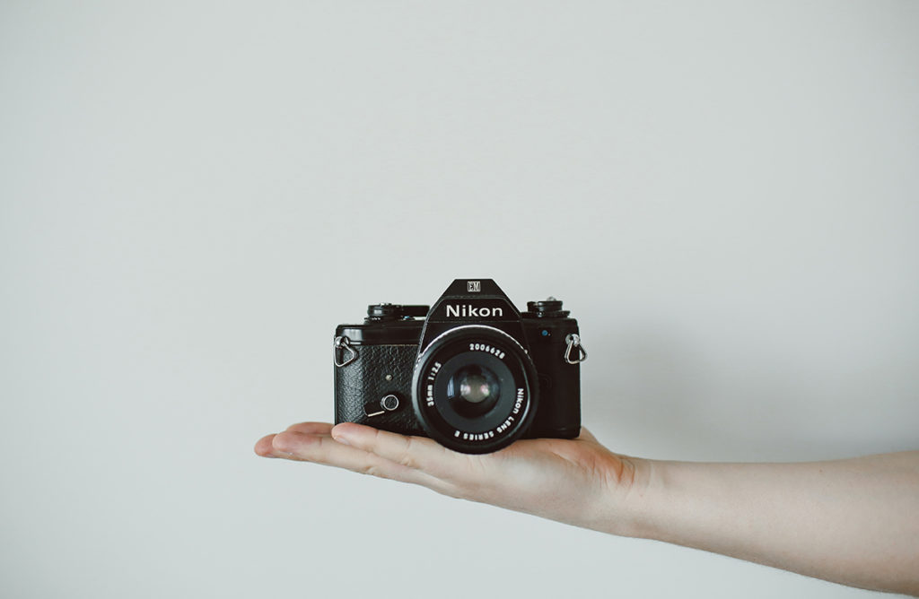 image of analogue Nikon camera resting on hand in front of white wall.