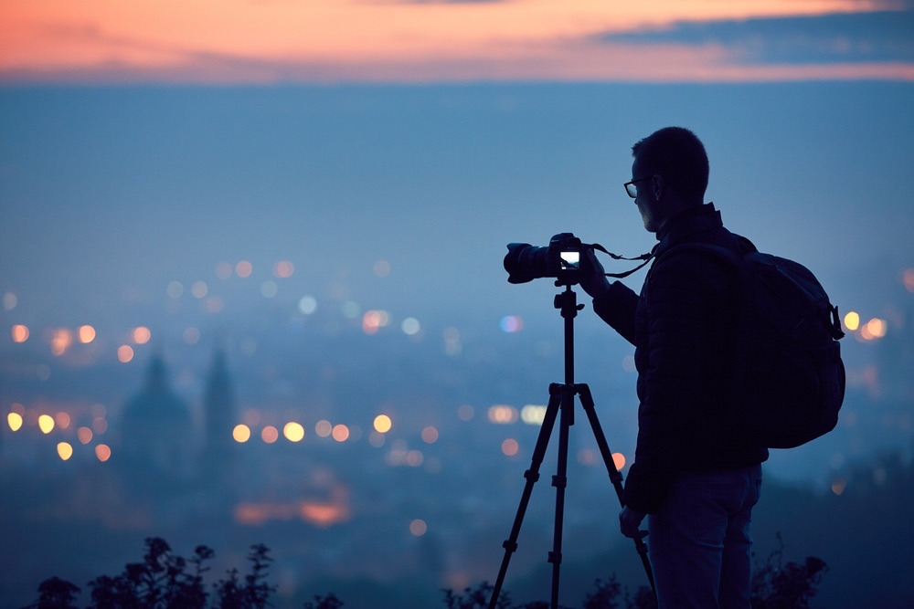 A young male photographer using his camera on a tripod in low light photography.