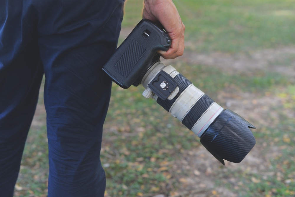 A photographer carrying a full-frame kit including a large telephoto lens. Handheld telephoto photography.