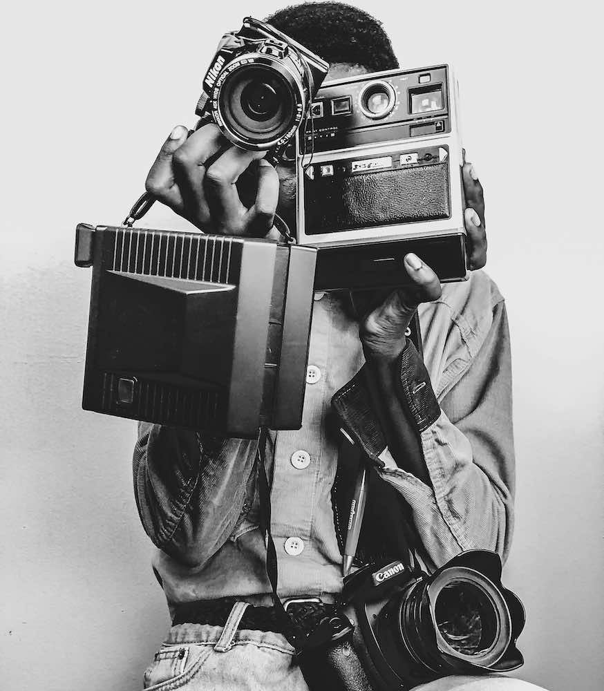 black & white photo of person holding different cameras.