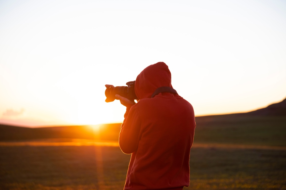 A lone photographer is aiming a camera at a scene during sunrise.