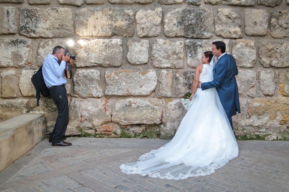 A wedding photographer aims his flash at an upward angle while photographing a bride and groom.