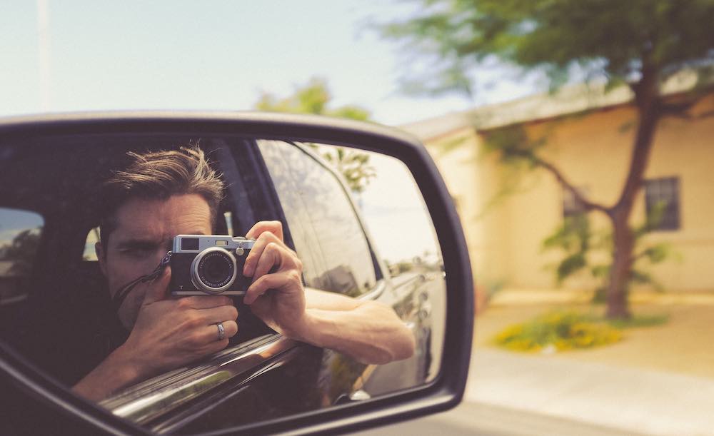man taking self-portrait in rearview mirror.