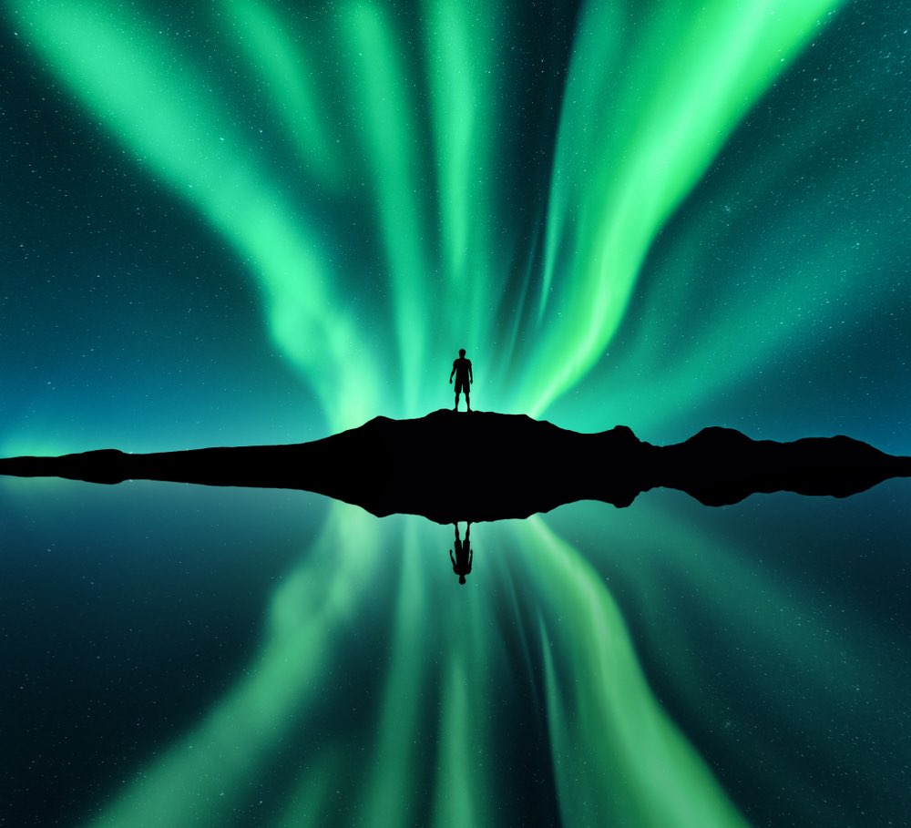 Man standing in front of aurora borealis in Lofoten Islands, Norway.