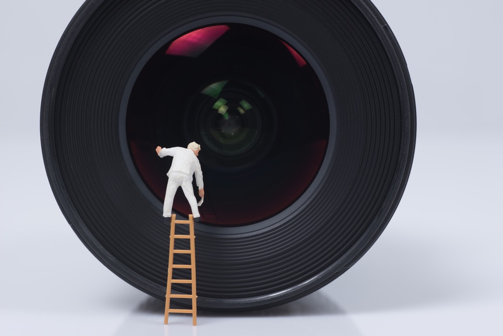 A miniature figurine on a ladder 'cleaning' a macro lens. Creative miniature photography composition incorporating camera equipment as a prop.