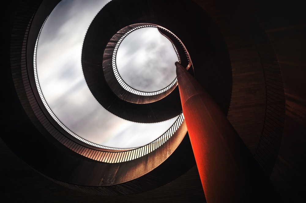 Architectural photography of a spiral staircase structure on a cloudy day. Low-angle photo employing overt leading lines.