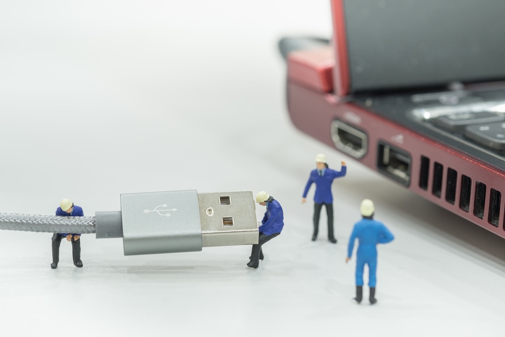 A group of miniature workers attempting to connect a USB cable to a laptop's port. An example of how composition and storytelling can connect miniature props with life-sized ones.