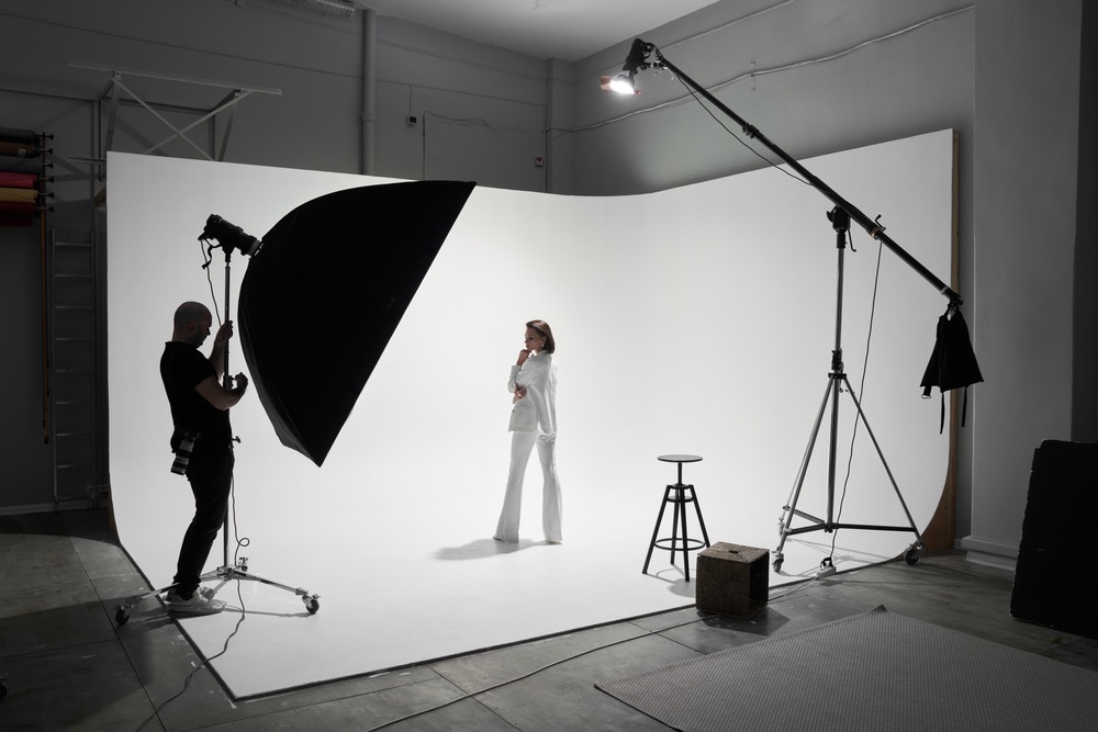Studio fashion photography. Inside of a professional photography studio setup with lighting equipment and crew. Female model in center.