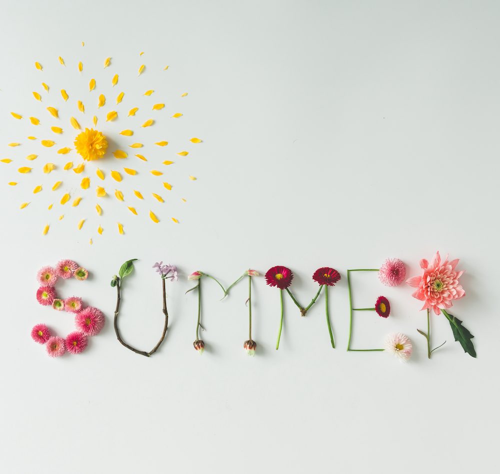 "summer" spelled using flower petals and flower stems on a white table.